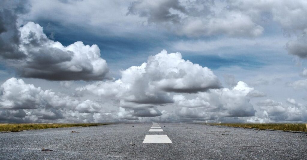 A straight road stretched toward a dramatic sky filled with fluffy clouds, creating a sense of journey.