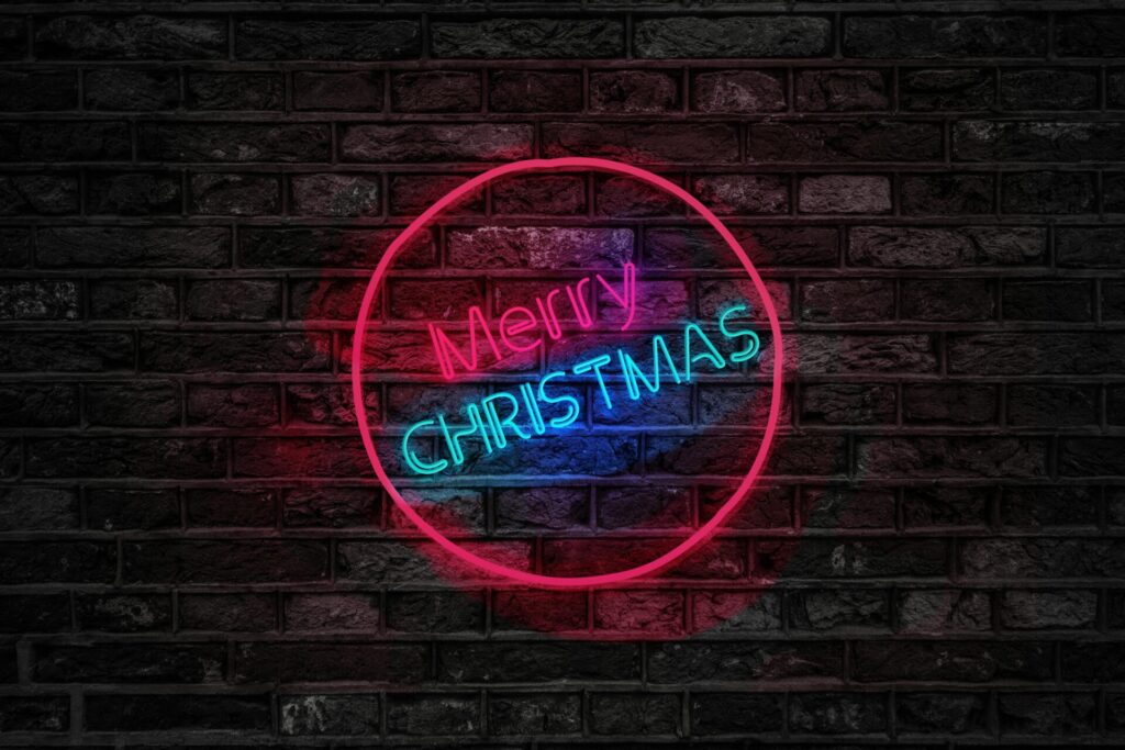 Vibrant neon Merry Christmas sign glowing on a dark brick wall, perfect for holiday themes.