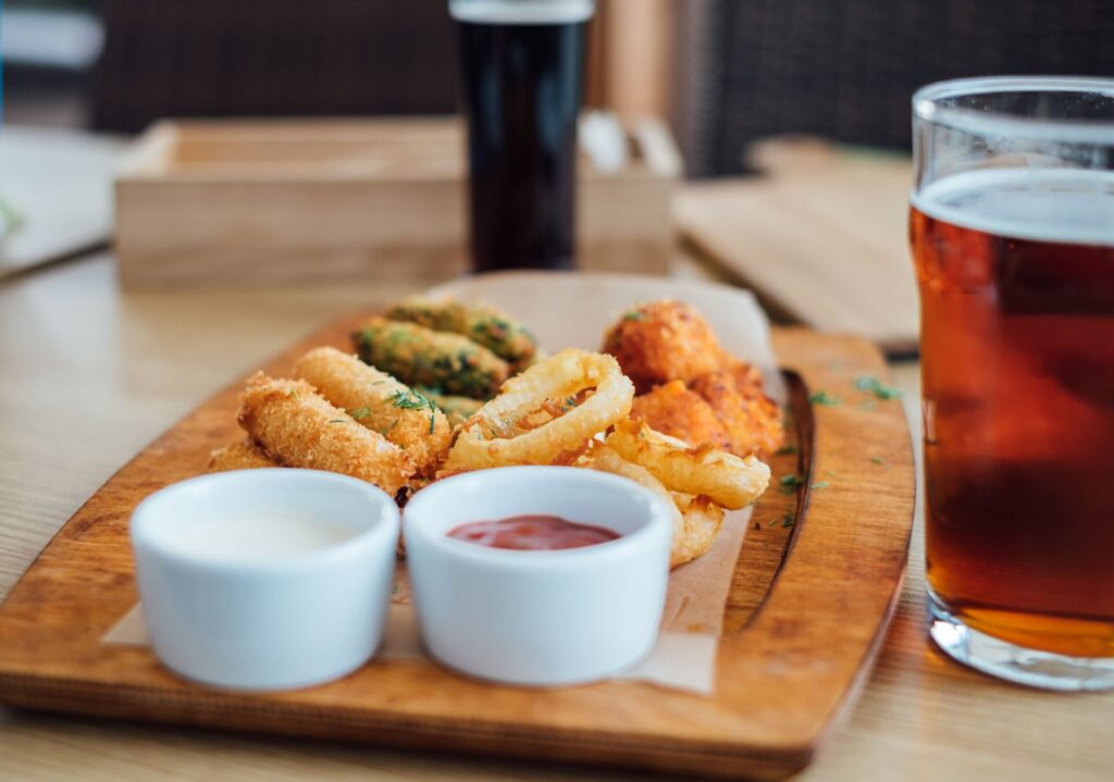 A variety of appetizers with dipping sauces served with beer on a wooden platter indoors.